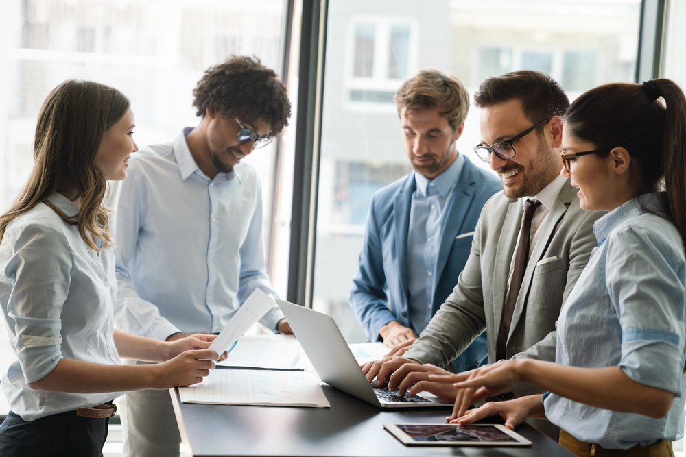 A team of professionals reviewing work together around a laptop