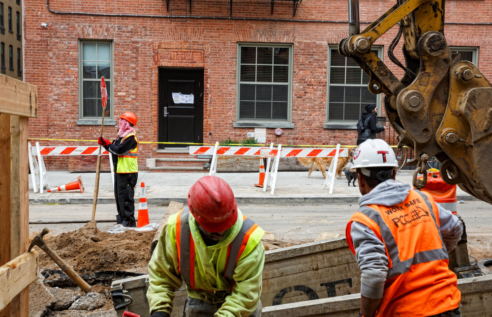 Construction crew in hard hats and safety vests working at a street excavation site