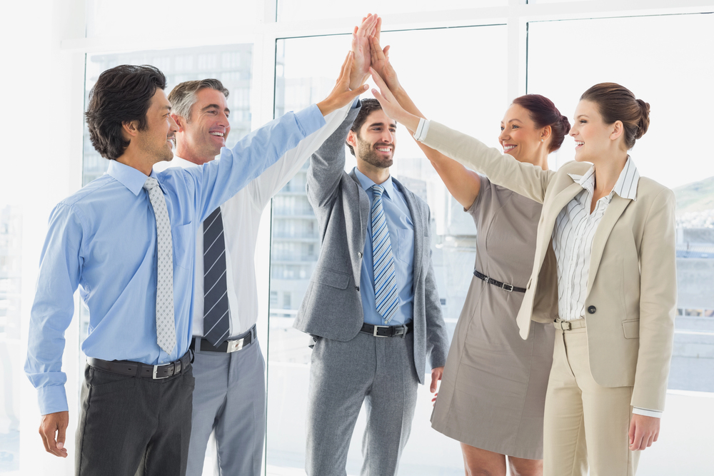 A team of business professionals sharing a group high-five in a bright office