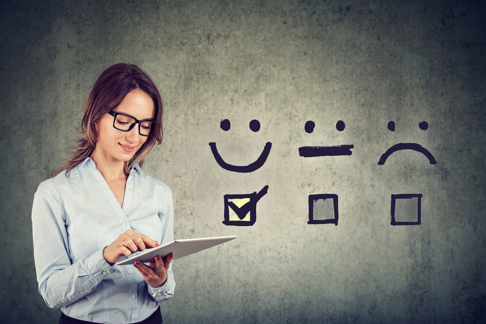 A woman using a tablet beside chalk-drawn satisfaction ratings on a wall