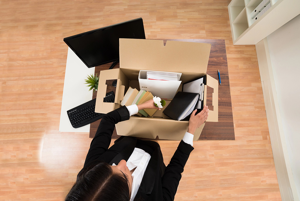 A manager packing personal belongings into a cardboard box at her desk
